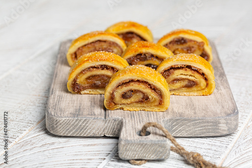 Close-up of homemade filled pastries - cut rugelach cookies. Made with butter and cream cheese doughs filled with apricot, raisins and walnuts, on white wooden table. photo