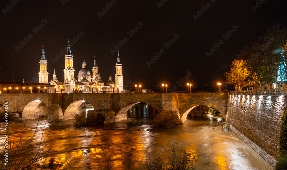 Obraz premium Long exposure at night on the Puente de Piedra next to the Basilica of Nuestra Señora del Pilar on the Ebro river in the city of Zaragoza, Aragon. Spain