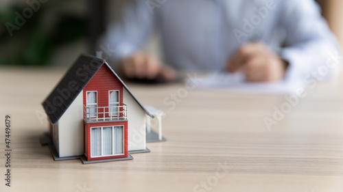 On blurred background, client sits at table signing rental agreement or purchasing contract, close up to cottage house layout. New built house offer, affordable dwelling, real-estate agency ad concept