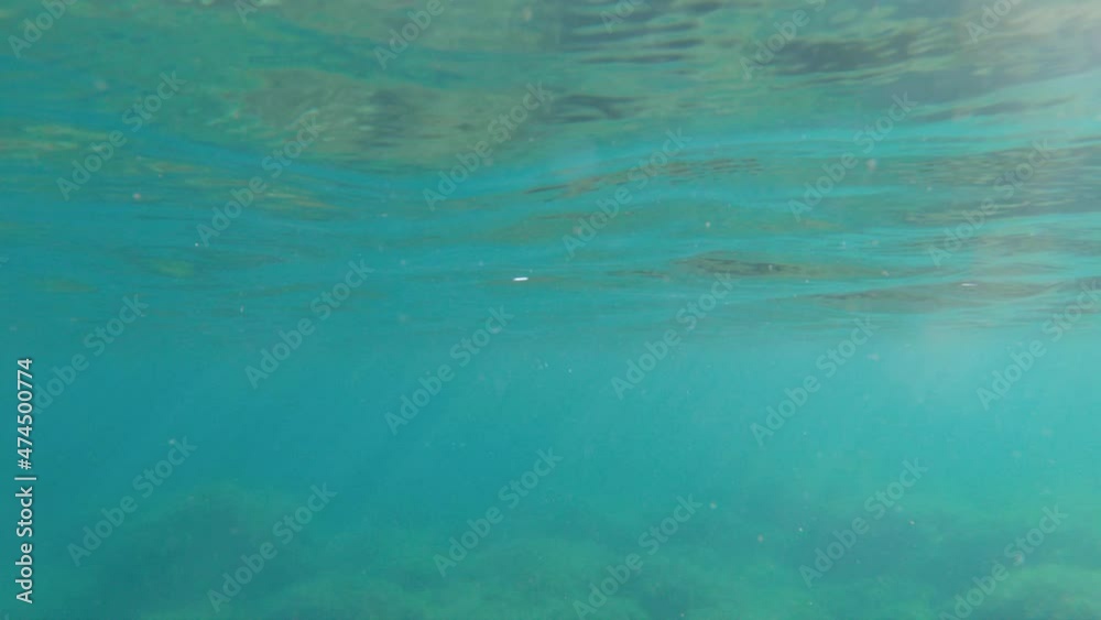 Beneath the surface view of the underwater sea with natural rays of light shining through the shiny and moving surface of the water, caustics, bubbles and foam Beneath the surface view of the underwater sea with natural rays of light shining through the shiny and moving surface of the water, caustics, bubbles and foam