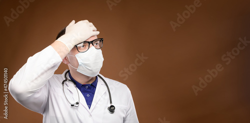 panoramic Young caucasian doctor in a medical uniform makes a facepalm gesture. Medical errors and stupidity