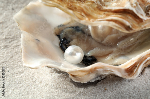 Open oyster with white pearl on sand, closeup