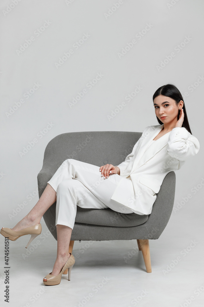 Good looking business woman on a grey armchair smiling and looking at camera Good looking business woman on a grey armchair smiling and looking at camera