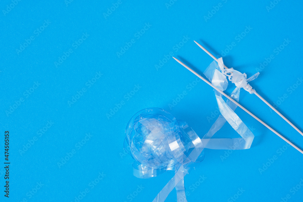 Naklejka premium recycled plastic yarn concept, knitting needles, chopped plastic balls on bright blue background