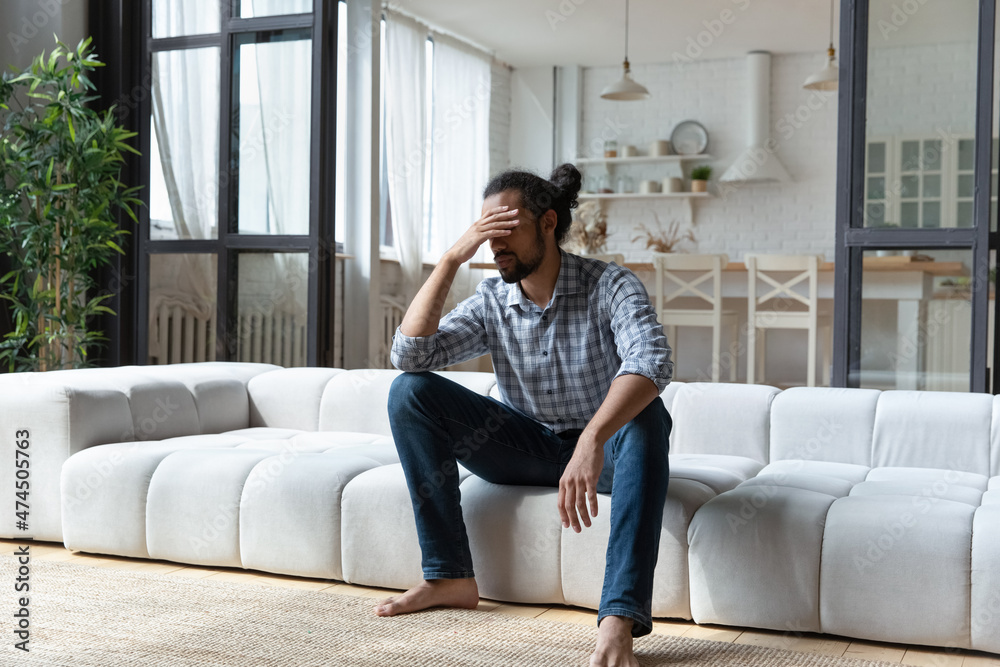 Young African guy sit on sofa at home touch head looks desperate, suffers from headache, goes through divorce feel mental pain, depressed due to hard life situation, break up, personal trouble concept Young African guy sit on sofa at home touch head looks desperate, suffers from headache, goes through divorce feel mental pain, depressed due to hard life situation, break up, personal trouble concept