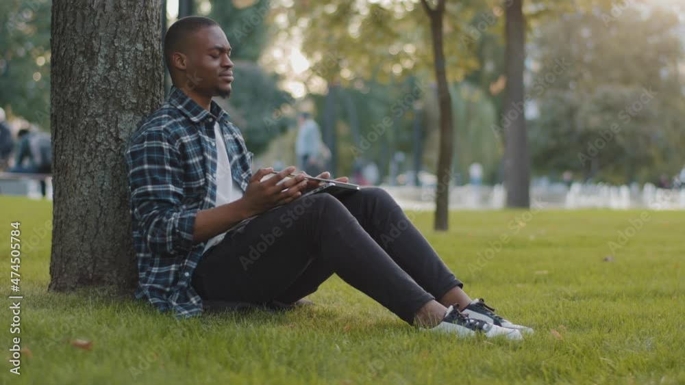 Tired student guy bored male african american business man freelancer sitting on green grass lawn in park feeling neck pain discomfort closes laptop stop work learning resting relaxing taking break