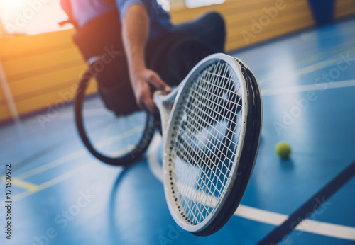 Adult man with a physical disability who uses wheelchair playing tennis on indoor tennis court © romaset