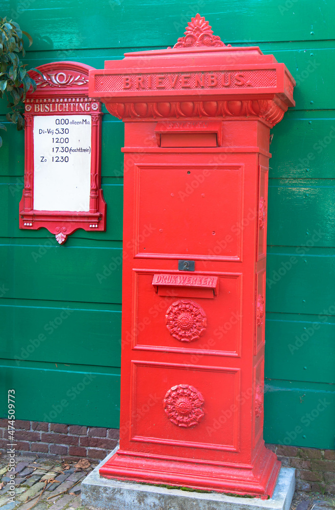 Traditional red dutch post box in front of green wall. Retro style red mailbox in historic village Arnhem, Netherlands Traditional red dutch post box in front of green wall. Retro style red mailbox in historic village Arnhem, Netherlands