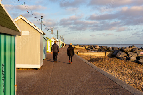 Beach huts in Felixstowe, Suffolk, England with an unknown elderly couple walking away from camera