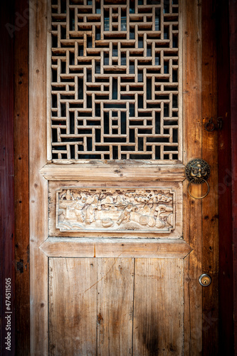Close-up detail of ancient classic wooden door panel decorated with typical Chinese architecture style pattern and woodcarving with old metal doorknob installed at an old house in China