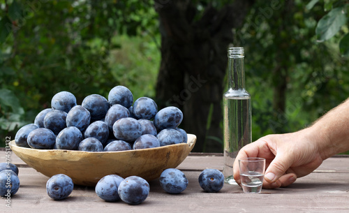 Wooden bowl of garden plums and plum brandy drink in shot glasses on old wooden table with a tablecloth, copy space.