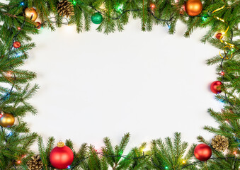 Christmas frame made of fir branches baubles cones and Christmas multicolored electric lights on white background