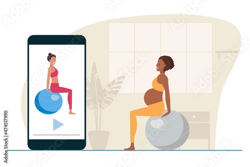Online Exercises with fitball for pregnant women. Pregnant African American sitting on large gray ball at home. Woman watches at sport lessons on your phone. Prenatal Exercises, healthy lifestyle.