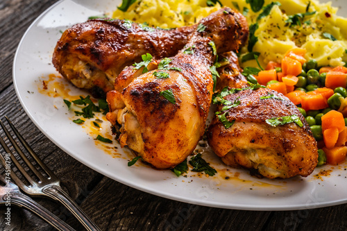 Barbecue chicken drumsticks with potato puree, green peas and carrot on wooden table