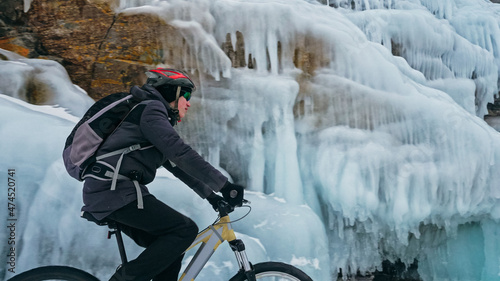 Man is riding bicycle near ice grotto. Rock with ice caves icicl © ivandanru