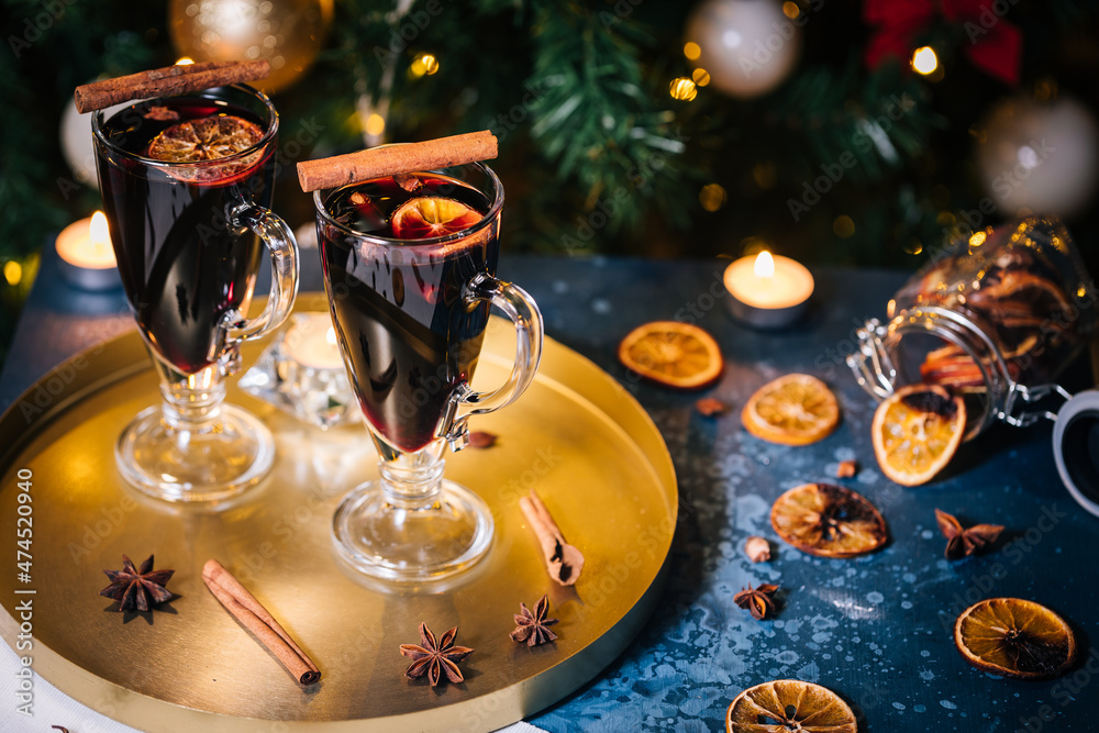 Mulled wine with cinnamon, anise star and orange served in festive Christmas decoration in front of a Christmas tree and lights. Ideal drink for advent and celebration.