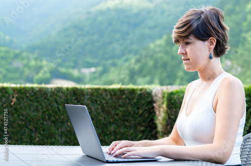 Fotografie Young adult woman working remotely with her laptop in a rural area