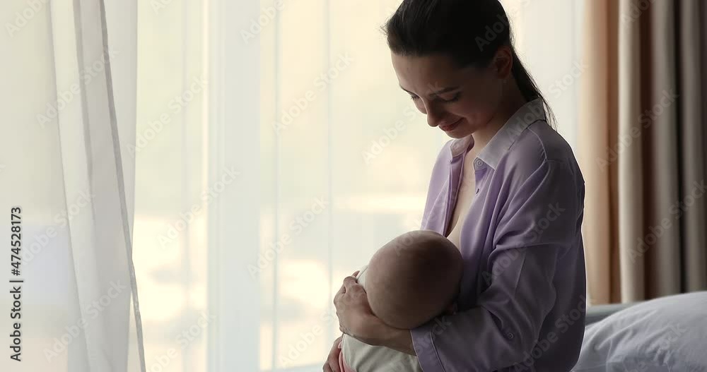 Pure affection. Tender millennial mom stand by window with light smile