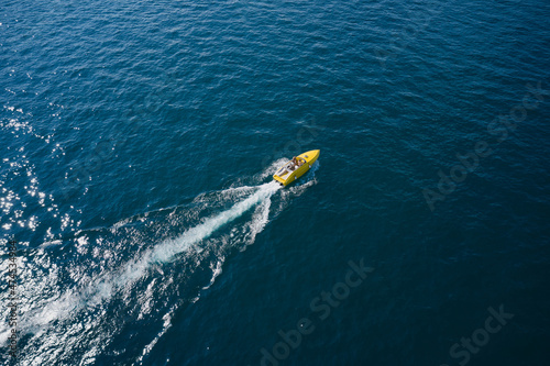 High-speed luxury yellow boat with people moving on dark blue water. Boat performance movement on the water aerial view.