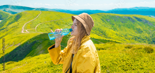 Young woman drinking bottle of water outdoors on the top of the mountain. Carpathians, Ukraine photo