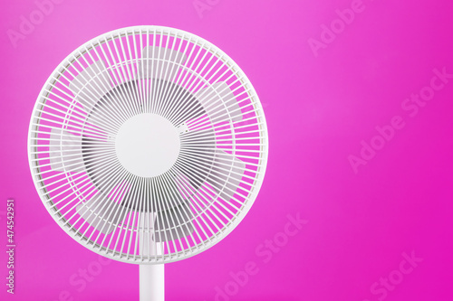 White modern electric fan for cooling the room on a pink background.