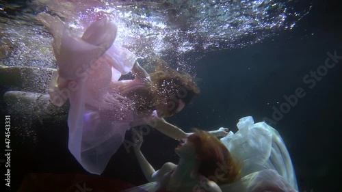 Two graceful women, swimming underwater in a gorgeous dress, a lady participates in an artistic performance