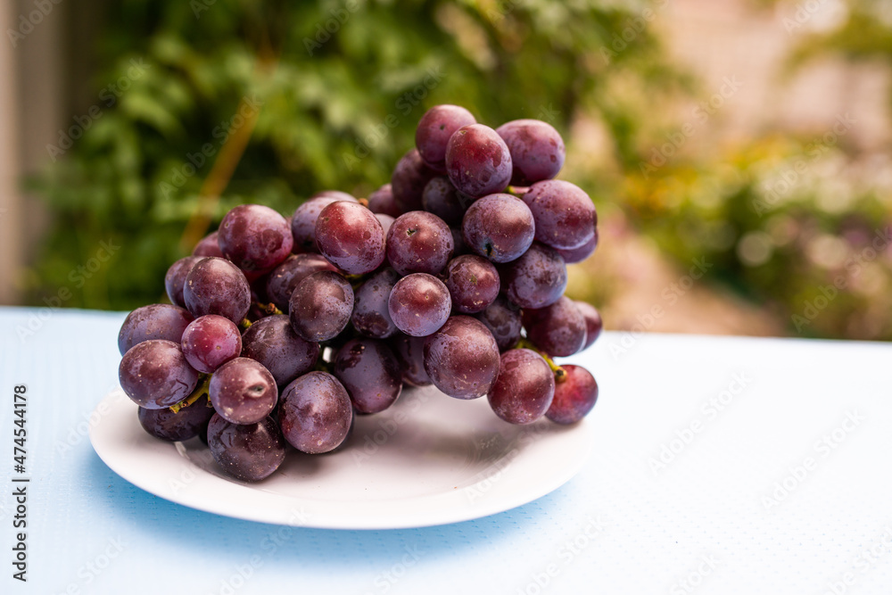 Fototapeta premium Ripe blue grape berries cluster on plate standing on table