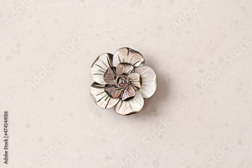 A flower brooch made of natural gray mother-of-pearl lies on a light modern gray white concrete background. Jewelry for women on a light background