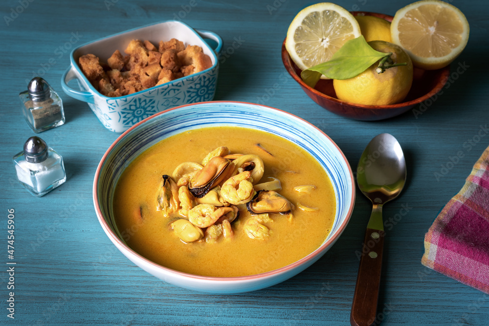 Seafood soup, based on prawns, mussels, clams, hake and squid, accompanied with pieces of fried bread, on a light blue wooden table. Seafood soup, based on prawns, mussels, clams, hake and squid, accompanied with pieces of fried bread, on a light blue wooden table.
