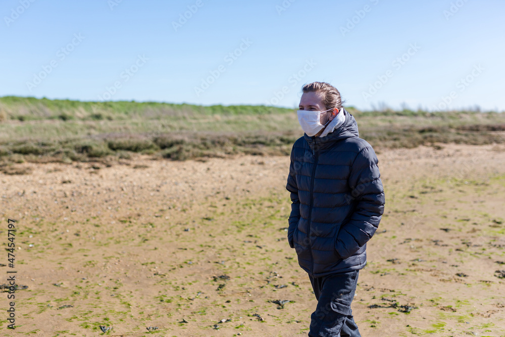 Man wearing a protective face mask walks his dog along a beach on his hours daily allowance for exercise that the government has allowed during the corona pandemic