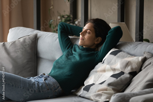 Happy calm Hispanic young woman sit relax on cozy sofa in living room dream or take nap at home. Peaceful millennial Latino female rest on couch sleep, relieve negative emotions. Peace concept. photo
