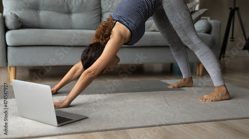 Healthy millennial Hispanic woman do morning stretching or pilates have webcam video training on computer at home. Sporty Latino female meditate engaged in distant yoga class online on laptop.