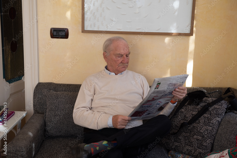 bellissimo nonno dai capelli bianchi che legge il quotidiano sul divano di casa - obrazy, fototapety, plakaty 
