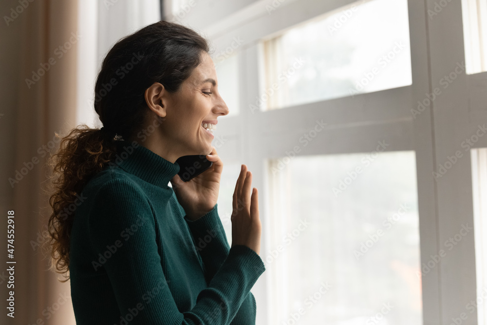 Happy young Latino woman talk speak on cellphone gadget look in window wave greeting with friend. Smiling Hispanic female on lockdown quarantine at home have smartphone call. Communication concept. Happy young Latino woman talk speak on cellphone gadget look in window wave greeting with friend. Smiling Hispanic female on lockdown quarantine at home have smartphone call. Communication concept.