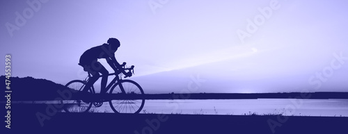 Nie do poznania sylwetka człowieka, jazda na rowerze przed zachodem słońca niebo. Trening rowerzystów na rowerze szosowym, jazda na rowerze wyścigowym na otwartej drodze. Stonowany w modnym Kolorze Roku 2022 Bardzo Peri.. Kopiowanie miejsca, baner