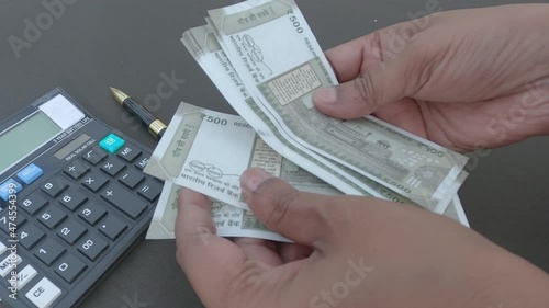 Human hand counting new 500 rupee indian currency note against a calculator and a pen placed on table. High angle view. Close up. Banking Business Finance Background.