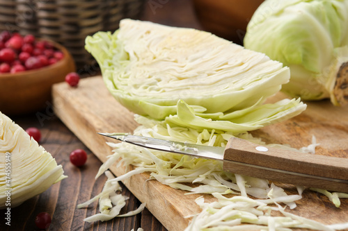 Chopped cabbage on a cutting board for making sauerkraut, coleslaw, salad or other cabbage dish. Bowl of cranberries on background.