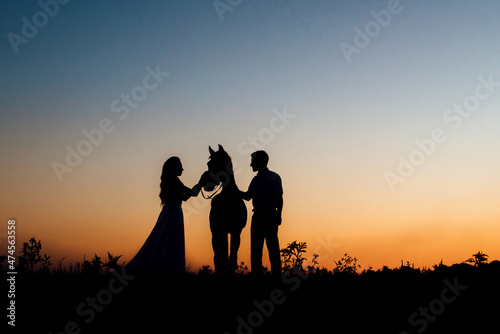 Silhouettes of a bride in a white dress and a groom in a white shirt on a walk