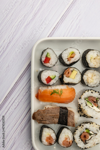 Teilausschnitt von Sushivarianten ordentlich angerichtet auf einen Teller mit weißem Holzuntergrund