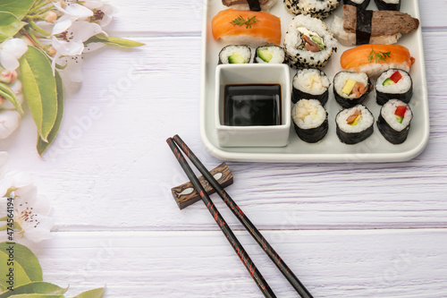 Diverse selbstkreierte Sushivarianten ordentlich hergerichtet auf einen Teller mit weißem Holzuntergrund und Blumendekoration photo