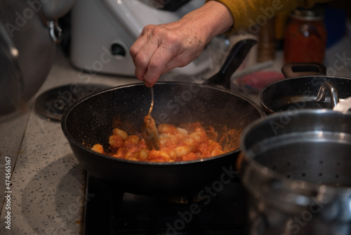 mani che mescolano gnocchi al pomodoro casalinghi in padella photo