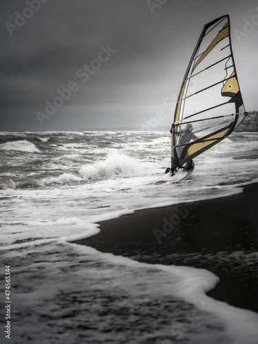 Canvas Print wind surfer with sail on the beach entries into water at storm sea