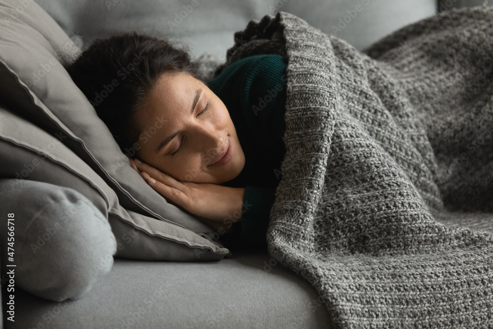 Happy calm millennial Latino woman lying relaxing on sofa under warm blanket feel cozy relaxed at home. Peaceful young Hispanic female rest on couch sleep or take nap. Relaxation, fatigue concept. Happy calm millennial Latino woman lying relaxing on sofa under warm blanket feel cozy relaxed at home. Peaceful young Hispanic female rest on couch sleep or take nap. Relaxation, fatigue concept.