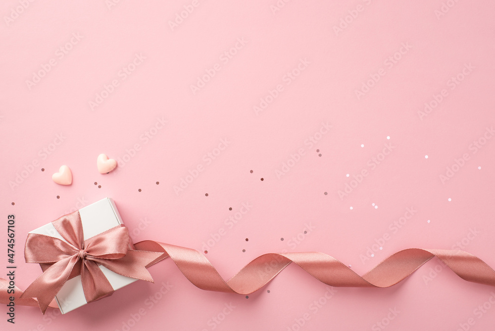 Top view photo of st valentine's day decorations white giftbox with bow pink curly ribbon small hearts and sequins on isolated pastel pink background with empty space