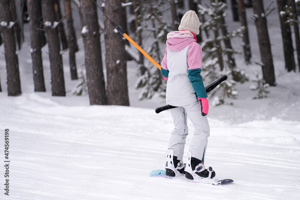 Winter sports recreation. A young woman standing on a board climbs uphill on a rope lift. Copy space. Winter sports recreation. A young woman standing on a board climbs uphill on a rope lift. Copy space.
