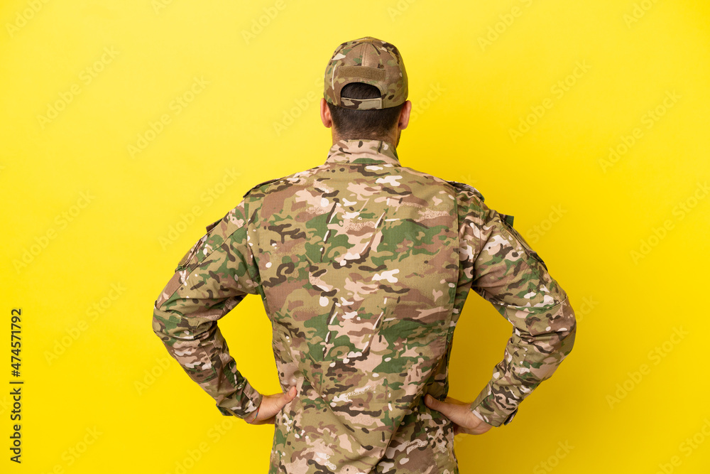 Military man isolated on yellow background in back position Military man isolated on yellow background in back position