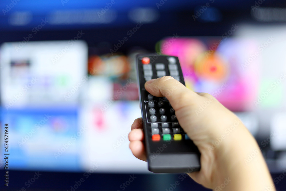 Female hand with remote controller on smart TV screen background. Woman choosing streaming services, watching movies Female hand with remote controller on smart TV screen background. Woman choosing streaming services, watching movies