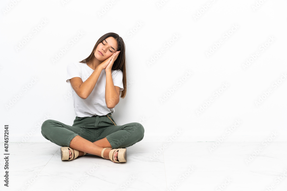 Teenager girl sitting on the floor making sleep gesture in dorable expression Teenager girl sitting on the floor making sleep gesture in dorable expression