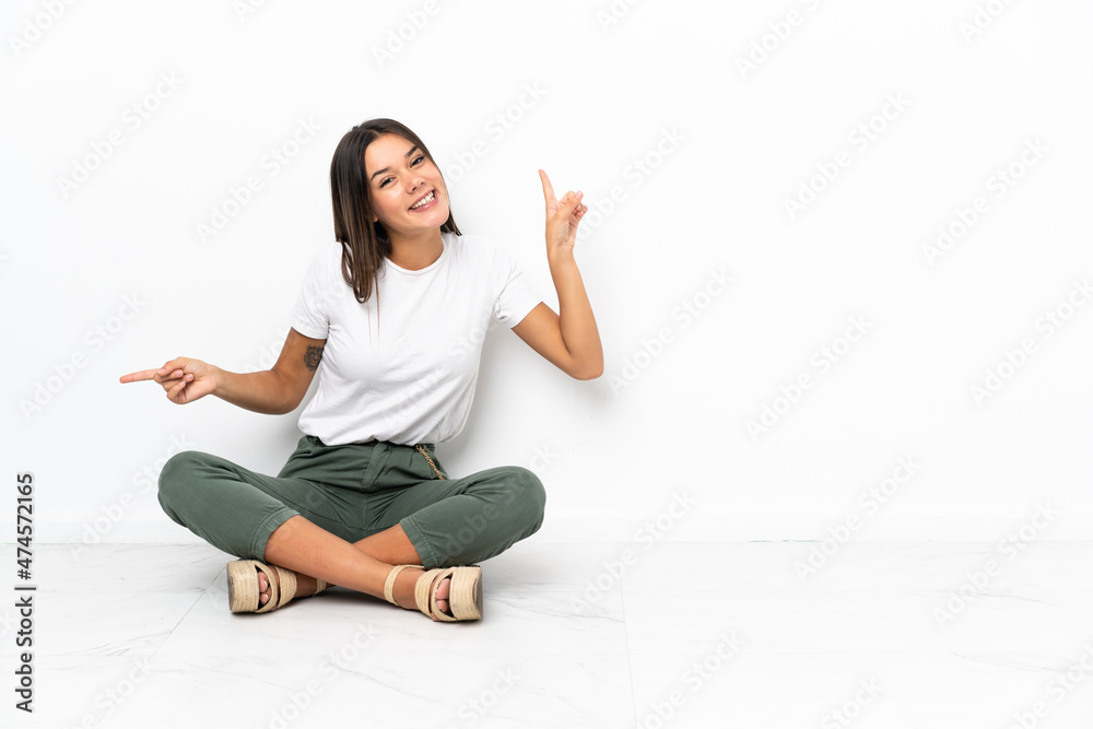 Teenager girl sitting on the floor pointing finger to the laterals and happy Teenager girl sitting on the floor pointing finger to the laterals and happy