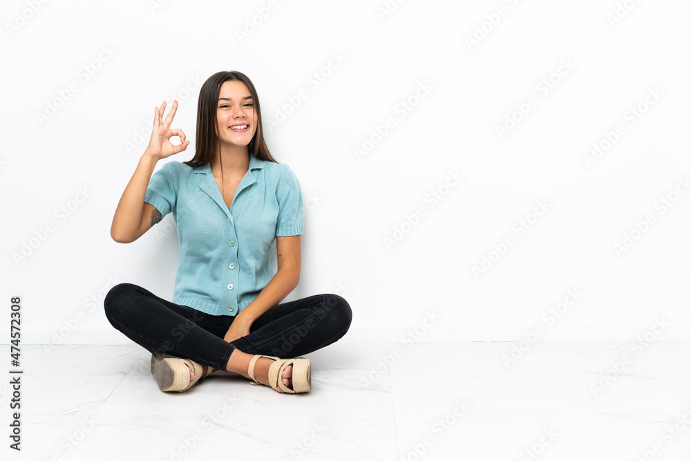 Teenager girl sitting on the floor showing ok sign with fingers Teenager girl sitting on the floor showing ok sign with fingers